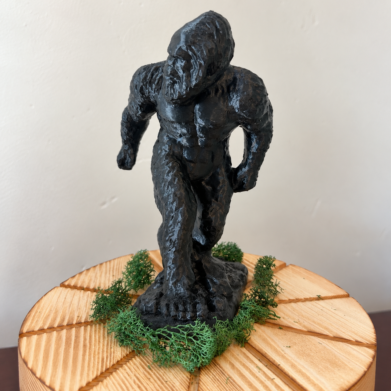 Black 3D-printed Bigfoot figurine standing on a wooden display with moss